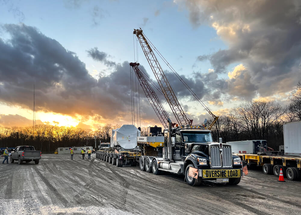 Sunset view with a Buckingham truck and trailer transporting a wind turbine component in the foreground