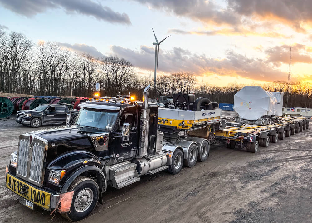 A loaded Buckingham semi and trailer with wind turbine components at sunset